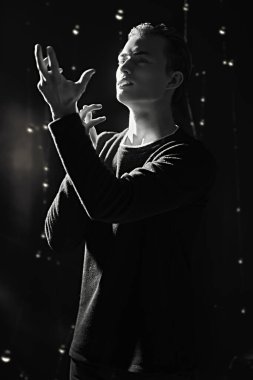 Yakışıklı genç adam ışığa bakar ve elleriyle ilham verici bir şey gösterir. Duygular ve duygular. Siyah-beyaz portre. 