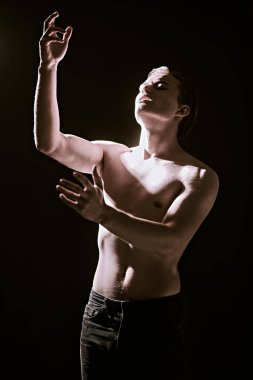 Mükemmel kaslı vücudu olan ve ellerini ışığa doğru uzatan yakışıklı bir genç adamın portresi. Sanat portresi. Erkeklerin güzelliği ve sağlığı.