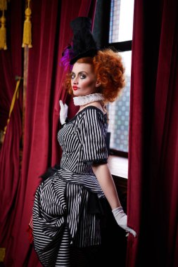 Yakışıklı palyaço kız perdelerin arkasından bakıp gülümsüyor. Retro biçimi.