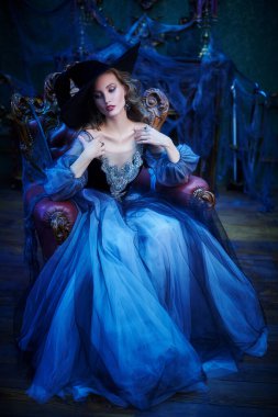 Eski kaledeki koltukta oturan şapkalı ve güzel elbiseli çekici bir cadının portresi. Cadılar Bayramı. Kutlama.