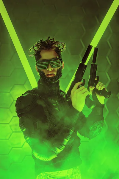 Warrior of the future. A brave cyberpunk warrior in protective uniform stands on alert with weapons in his hands in neon light. Game, virtual reality.