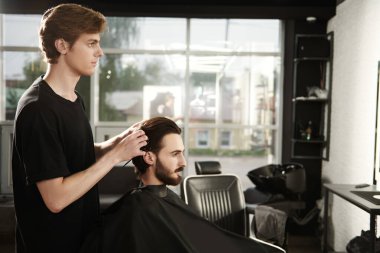 Berber dükkanında müşteriye hizmet eden kuaför. Yakışıklı esmer adam kuaför salonunu ziyaret ediyor..