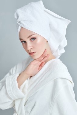 Güzellik, vücut bakımı, spa. Beyaz bornozlu güzel bir genç kadın portresi ve duş aldıktan sonra saçının etrafına bir havlu.. 