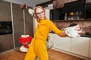 Parlak sarı tulumlu çekici genç bayan evde, mutfakta kahve yapıyor. Modern iç mekan, mutfak için mobilya. Ev yemeği.. 