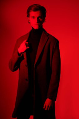 Erkek tarzı. Stüdyoda kırmızı ışıkta poz veren zarif elbiseli yakışıklı bir gencin portresi..