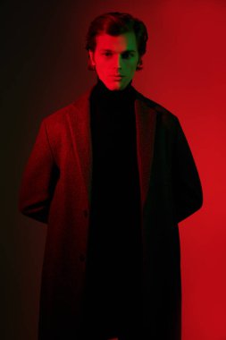 Zarif kıyafetler içindeki yakışıklı adam stüdyoda kırmızı ve yeşil ışıkta poz veriyor. Erkek güzelliği. Moda..