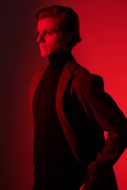 Portrait of a serious handsome man in elegant clothes posing at studio in red light. Men's beauty. Fashion.