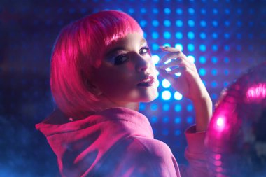Disko tarzı. Parlak makyajlı ve pembe saçlı modern kız gece kulübünün neon ışıklarında poz veriyor. Gece partisi tarzı.. 