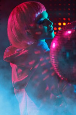 Gece partisi tarzı. Parlak makyajlı ve gece kulübünün neon ışıklarında poz veren pembe saçlı modern bir kız portresi. Disko biçimi. 
