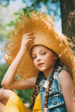Hasır şapkalı şirin bir kızın portresi parkta yürüyor ve kameraya gülümsüyor. Mutlu yaz tatilleri.. 