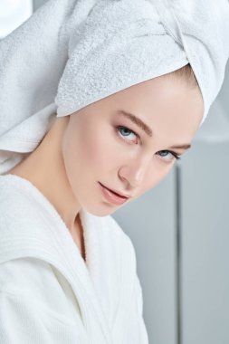 Beyaz bornozlu güzel bir genç kadının yakın plan portresi ve duş aldıktan sonra saçının etrafına bir havlu. Güzellik, vücut bakımı, kaplıca. 