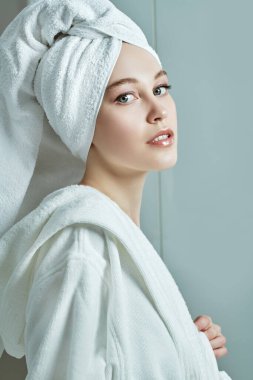 Güzellik, vücut bakımı, spa. Beyaz bornozlu güzel bir genç kadın portresi ve duş aldıktan sonra saçının etrafına bir havlu.. 