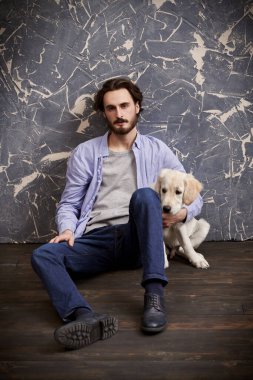 Golden Retriever köpeğiyle yerde oturan genç bir adamın tam boy portresi. Bir adam ve bir evcil hayvan.