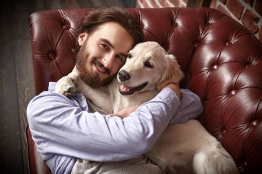 Mutlu genç adam evdeki kanepede evcil köpeği Golden Retriever ile oynuyor..
