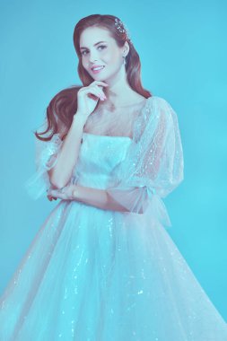 Düğün stili. Lüks beyaz elbiseli, yumuşak mavi ışıklı güzel bir gelinin portresi. Düğün makyajı ve saç stili.