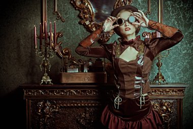 Steampunk dünyası. Victoria döneminden kalma iç mimarisi olan bir odada şöminenin yanında duran güzel bir steampunk bayanın portresi.. 