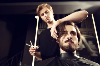 Berber dükkanında müşteriye hizmet eden kuaför. Yakışıklı esmer adam kuaförde kuaförü ziyaret ediyor..