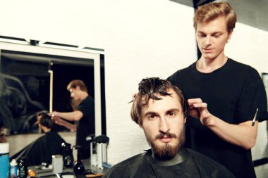 Berber dükkanı. Yakışıklı esmer adam berber dükkanında bir sandalyede otururken kuaföre saç kestiriyor.. 