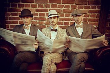 Retro tarzı. Zarif takım elbiseli üç yakışıklı deri koltukta oturup gazete okuyor. Gazete editörlüğü. Erkek modası. Erkekler kulübü.. 