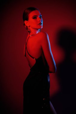 Zarif model kız stüdyoda kırmızı ışıkta parlak elbiseler içinde poz veriyor. Güzel dansçı kız. Güzellik, moda.