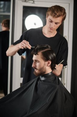 Yakışıklı esmer adam berber dükkanında bir sandalyede otururken kuaföre saç kestiriyor.. 