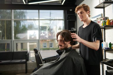 Berber dükkanında müşteriye hizmet eden kuaför. Yakışıklı esmer adam kuaför salonunu ziyaret ediyor..