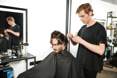 Kuaför salonu. Yakışıklı esmer adam berber dükkanında bir sandalyede otururken kuaföre saç tıraşı oluyor.. 