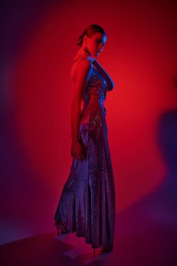 Zarif genç bayan dansçı zarif uzun elbiseler ve yüksek topuklularla poz veriyor. Kırmızı ışıkta tam boy stüdyo resmi.