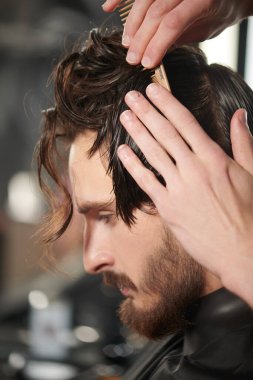 Berber dükkanı. Yakışıklı esmer adam berber dükkanında bir sandalyede otururken kuaföre saç kestiriyor.. 