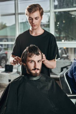 Berber dükkanında müşteriye hizmet eden kuaför. Yakışıklı esmer adam kuaför salonunu ziyaret ediyor..