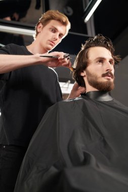 Kuaför salonu. Yakışıklı esmer adam berber dükkanında bir sandalyede otururken kuaföre saç tıraşı oluyor.. 