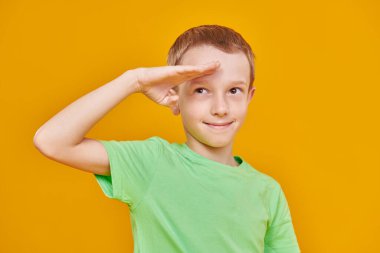 Komik neşeli çocuk uzaktan bakıp gülümsüyor. Çocuklar ve eğitim. Fotokopi alanı olan sarı bir arkaplanda stüdyo resmi.
