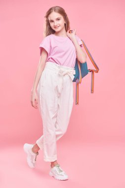 Hafif yaz kıyafetleri içinde kaygısız, güzel bir kızın uzun bir portresi stüdyoda pembe arka planda poz veriyor. Gençlik modası. 