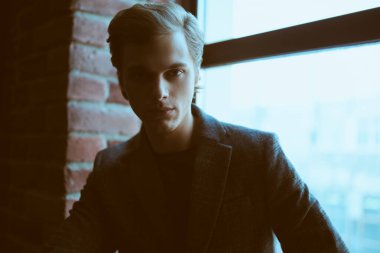 Çatı katındaki pencerenin yanındaki kameraya bakan ceketli yakışıklı bir gencin portresi. İş konsepti. 