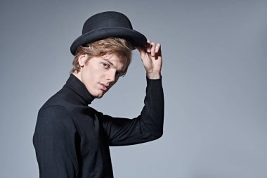 Siyah balıkçı yaka ve gri arka planda melon şapkalı yakışıklı bir gencin portresi. Erkek güzelliği. Moda.. 