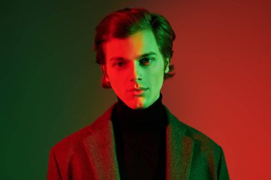 Stüdyoda renkli ışıkta şık kıyafetler içinde poz veren zarif bir gencin portresi. Moda fotoğrafı..