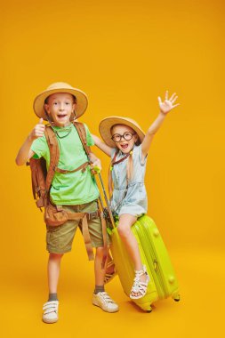 Funny children go on a journey. Summer vacation, tourism. Children's dreams and imaginations. Studio portrait on a yellow background. clipart