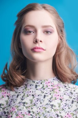 Romantik dalgalı saçlı, açık pembe makyajlı güzel bir kız mavi arka planda kameraya gülümsüyor. Yaz güzelliği.