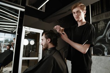 Yakışıklı esmer adam berber dükkanında bir sandalyede otururken kuaföre saç kestiriyor.. 