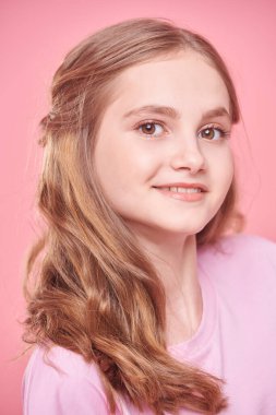 Olumlu duygular. Sarı saçlı, pembe tişörtlü güzel bir genç kız pembe arka planda kameraya gülümsüyor..  