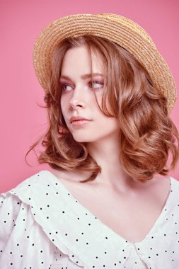 Açık beyaz yaz elbisesi içinde güzel bir kızın portresi ve pembe arka planda hasır bir şapka. Hafif romantik yaz tarzı. Güzellik, moda.