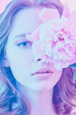 Güzellik ve çiçekler. Güzel bir kızın yakın plan portresi kıvırcık saçlı ve zarif mor menekşe makyajlı gözünün önünde narin bir şakayık çiçeği tutuyor. Güzellik, parfüm ve kozmetik.