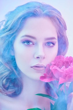 Zarif leylak-menekşe makyajlı güzel bir kadın hafif sisli şakayık bir çiçek tutuyor. Güzellik, parfüm ve kozmetik.