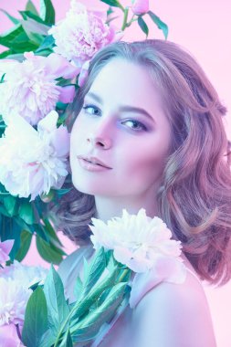 Çiçekler ve kadın güzelliği. Açık pembe arka planda narin şakayık çiçeklerinin arasında duran zarif leylak-menekşe makyajlı güzel bir kızın portresi. Güzellik, parfüm ve kozmetik.