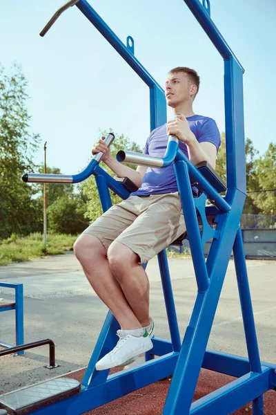 Sport, fitness, street workout concept. Athletic man doing abdominal exercises on sports equipment in the park.
