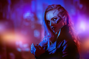 Güzel bir siber punk kızı geleceğin gece şehrinin arka planında duruyor. Siber punk konsepti. Teknoloji ve moda.