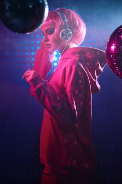 Disko tarzı. Parlak makyajlı ve gece kulübünde akıllı telefonunu tutan pembe saçlı modern bir kız. Karışık renk ışığı. 