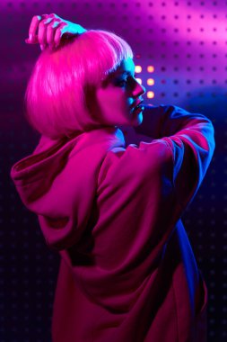 Gece partisi tarzı. Parlak makyajlı ve gece kulübünün neon ışıklarında dans eden pembe saçlı modern bir kız portresi. Disko biçimi. 
