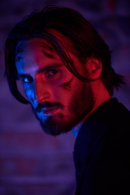Yaralı bir aksiyon kahramanının yakın plan portresi. Yüzünde kanlı yaralar var. Şehrin çok renkli ışıklarıyla.. 
