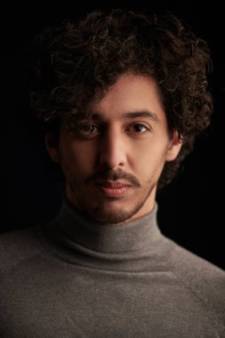 Siyah arka planda kıvırcık siyah saçlı yakışıklı bir gencin portresi. Erkeklerin güzelliği. 